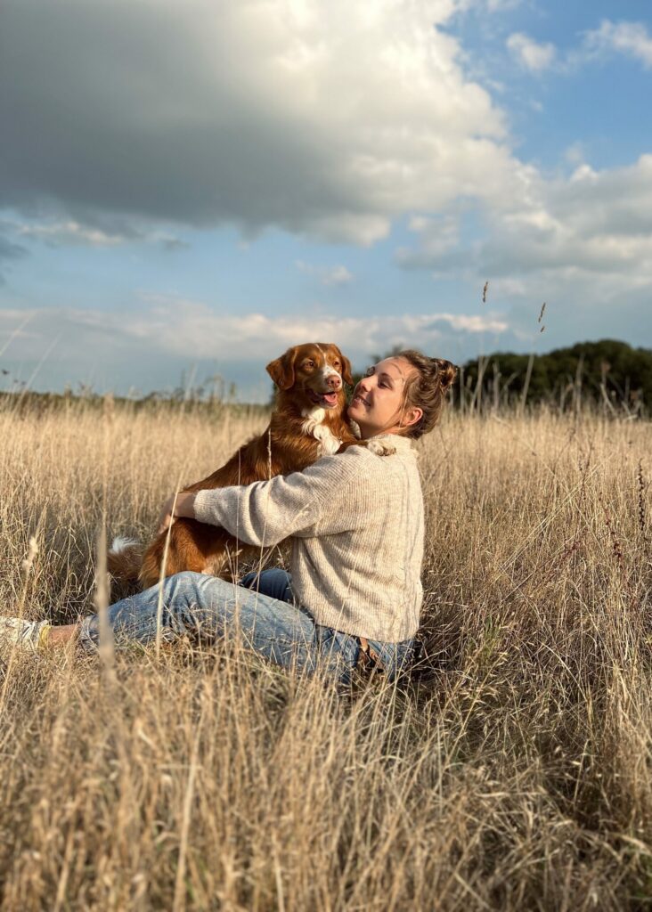 Margot GOULUT assise dans un champs avec un retriever de la nouvelle Ecosse dans les bras